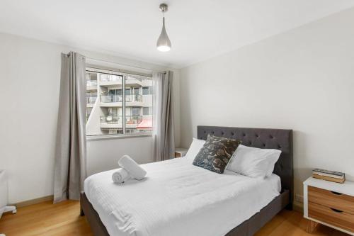 1 dormitorio con 1 cama blanca y ventana en 2-Bed Unit with Balcony BBQ & Stunning Lake Views, en Belconnen