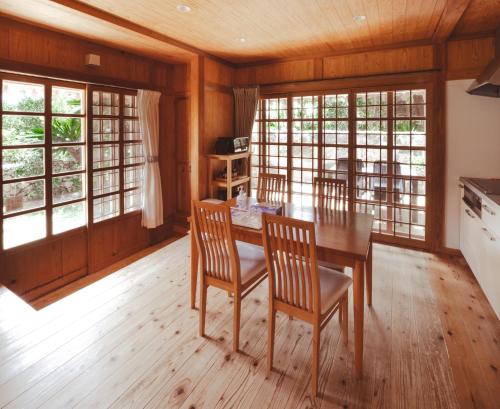 a dining room with a table and chairs and windows at かたあきの里 in Miyako Island