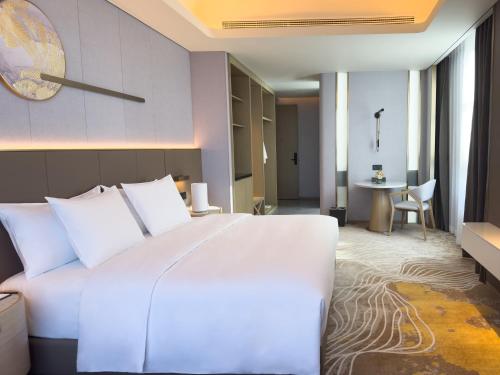 a bedroom with a large white bed and a table at Wanda Jin Jiamusi in Jiamusi