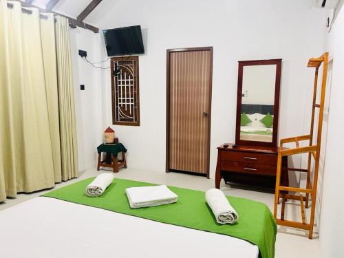 ein Schlafzimmer mit einem Bett mit einer grünen Decke und einem Spiegel in der Unterkunft Palm Beach Resort Ceylon in Jaffna