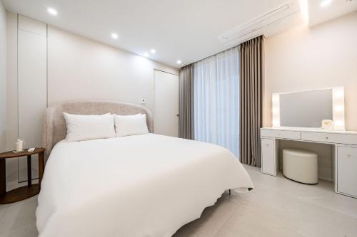 a white bedroom with a large bed and a desk at Brown Suites Busan Station in Busan