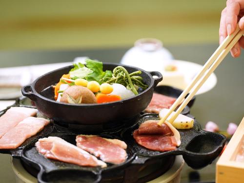 a skillet with meat and vegetables on a grill with chopsticks at 多武峰観光ホテル in Sakurai