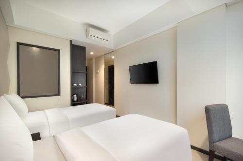 a bedroom with two white beds and a tv at Fashion Hotel Legian in Legian