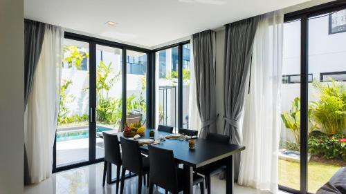 a dining room with a table and chairs and large windows at Laguna Park Villa in Phuket
