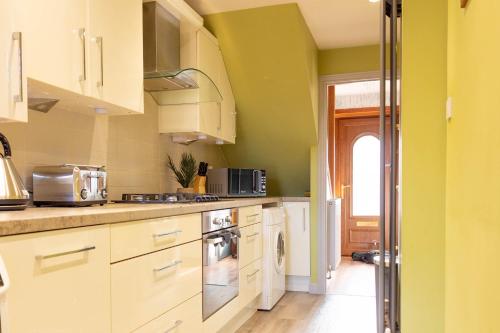 a kitchen with white cabinets and green walls at Gunn House in Grangemouth
