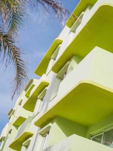 a white building with green balconies and a palm tree at Tropicana Ibiza Suites - Adults Only in Playa d'en Bossa