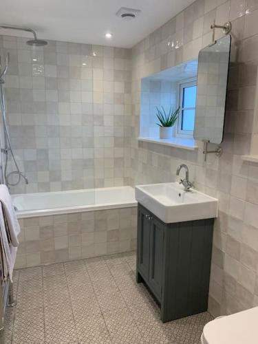 a bathroom with a sink and a tub and a mirror at Stunning East Devon Cider Barn in Northleigh