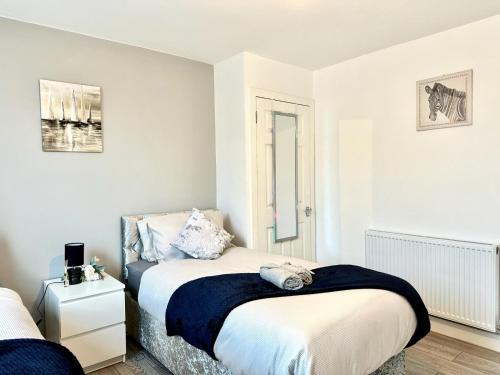 Cosy Modern 2 Bedroom Apartment bedroom with ensuite bathroom - Neath Road Port Talbot Near Briton Ferry Train Station في Briton Ferry: غرفة نوم بيضاء مع سرير وموقف ليلي