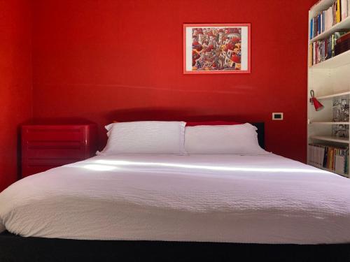 Dormitorio rojo con cama blanca y estante de libros en Draisina Bike ROOM en Oleggio Castello