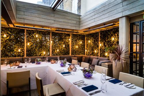 uma sala de jantar com mesas brancas, cadeiras e luzes em The Hari London em Londres
