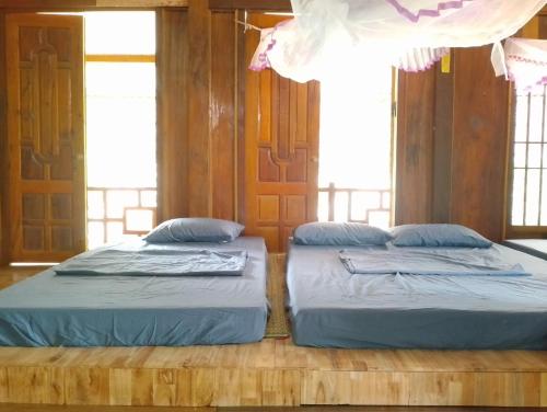 two beds in a room with wooden walls and windows at Du Gia Wooden Homestay in Làng Cac
