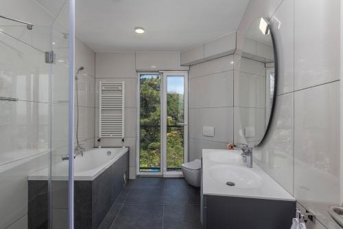 ein Badezimmer mit einer Badewanne, einem Waschbecken und einem Spiegel in der Unterkunft Villa Visum Mare Tribus in Mošćenička Draga
