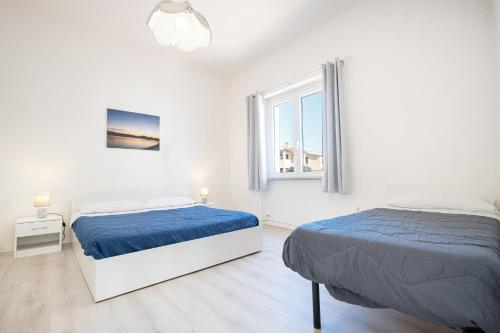 twee bedden in een witte kamer met twee ramen bij Appartamento Libeccio a 300m dalla spiaggia in Golfo Aranci