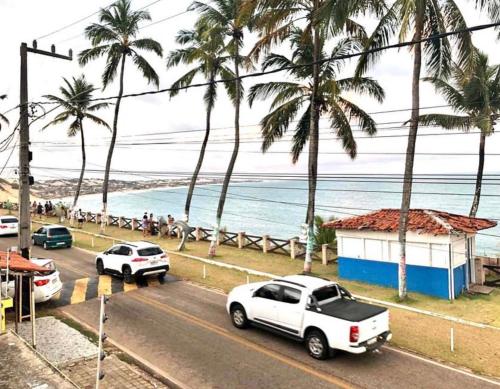 a street with parked cars and palm trees on the beach at AP Completo Tabatinga in Nísia Floresta