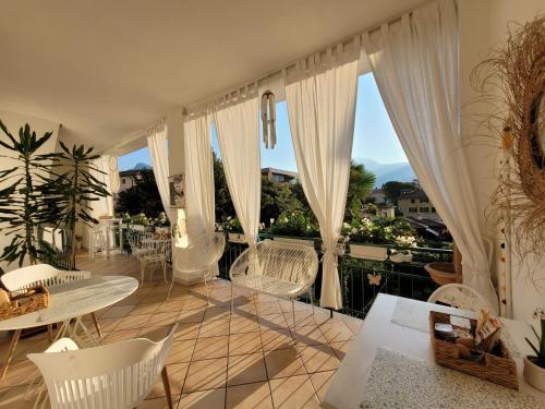 balcón con sillas blancas, mesas y ventanas en B&B Dal Nonno, en Riva del Garda