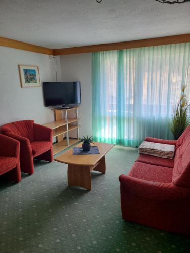 a living room with two red chairs and a flat screen tv at Hotel Residence in Grindelwald