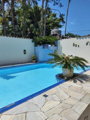 a swimming pool with plants next to a white wall at Paraíso NA PRAIA - CASA 3 SUITES MAX 8 PESSOAS in Bertioga