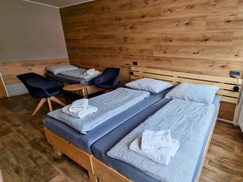 two beds and two chairs in a room with wooden walls at Penzion Pod Zámkem in Vizovice