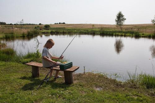 a person sitting on a picnic table with a fishing pole at Zielony-Bursztyn in Objazda-Kolonia