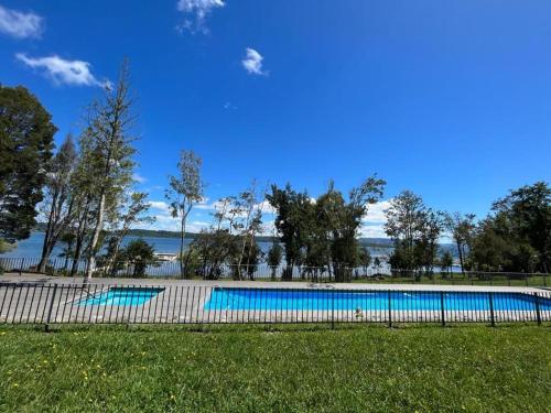 a swimming pool with trees and water in the background at Departamento Nuevo en Condominio La Puntilla Villarrica in Pucón