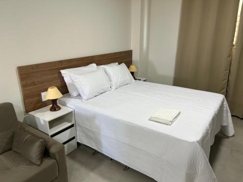 a bedroom with a white bed with a chair and a lamp at Condomínio Kaimã in Matinhos