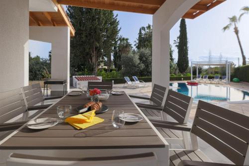einen Holztisch und Stühle auf einer Terrasse mit einem Pool in der Unterkunft Grand Villa Baci in Coral Bay