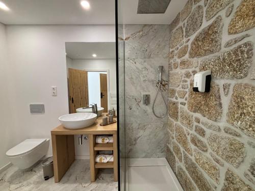 a bathroom with a sink and a toilet and a stone wall at Paços do Douro, Chambre privée avec piscine in Romariz