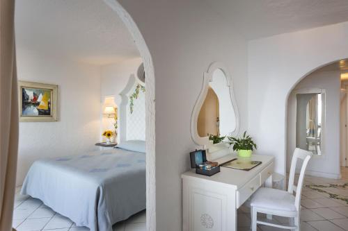a bedroom with a bed and a desk and a mirror at Hotel La Bisaccia in Baja Sardinia