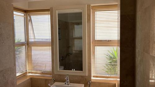 a bathroom with a sink and a mirror and windows at Calypso Beach Holiday House in Langebaan