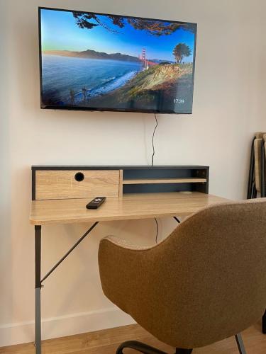 a desk with a television on a wall with a chair at Cocon zen du clocher - SOnights in Château-du-Loir