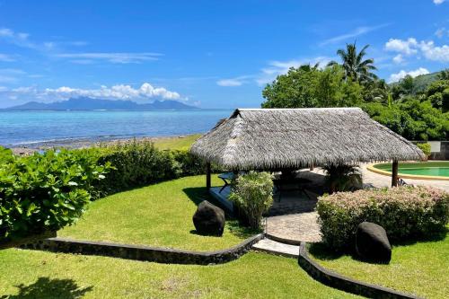 eine Hütte mit einem Grasdach auf einem Rasen in der Nähe des Wassers in der Unterkunft Kahaia beach home with pool amazing seafront black sand beach and reef in Paea