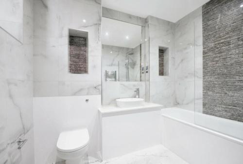 a white bathroom with a tub and a toilet and a sink at Stunning 2-Bed Apartment in Barking in Barking