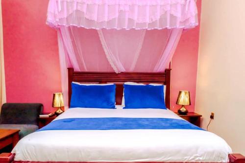 Dormitorio rosa con cama con almohadas azules en Beri Cottages, en Arua