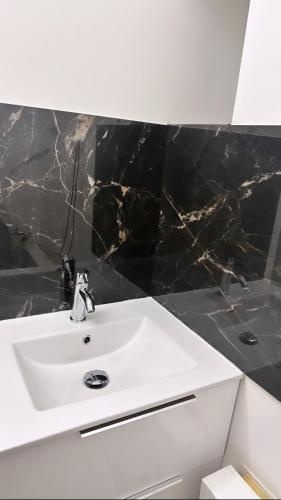 a bathroom with a white sink and black tiles at Chambres sur Cergy in Cergy