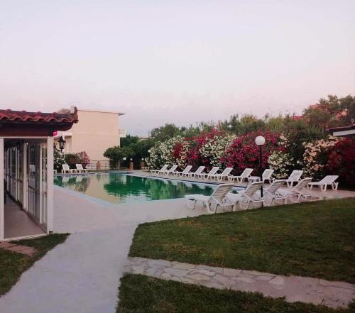 una piscina con tumbonas blancas junto a un edificio en Lunzi Verde, en Laganas