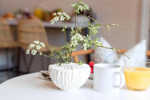 a white vase with flowers and a cup of orange juice at Poole Park House in Poole