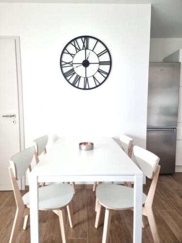 une table et des chaises blanches avec une horloge sur le mur dans l'établissement Le frontalier appart, à Saint-Louis