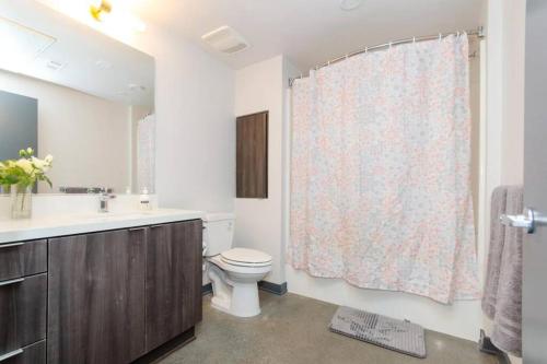 y baño con aseo, lavamanos y cortina de ducha. en Cozy 3bed Condo with balcony & a rooftop pool en Los Ángeles