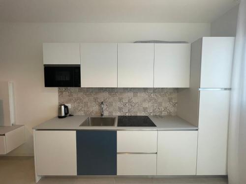 a white kitchen with a sink and a refrigerator at Woody Green Charming Apartments - Agenzia Cocal in Caorle