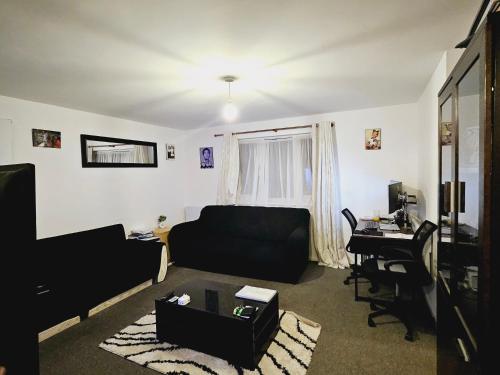 a living room with a black couch and a desk at Lovely Fully Furnished One Bed Flat To Let in Enfield Lock