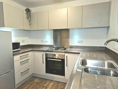 a kitchen with white cabinets and a stove and a sink at Modern & Fully Furnished in Bristol