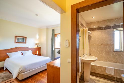 a bedroom with a bed and a tub and a sink at Hotel Ulveira in Oliveira de Frades