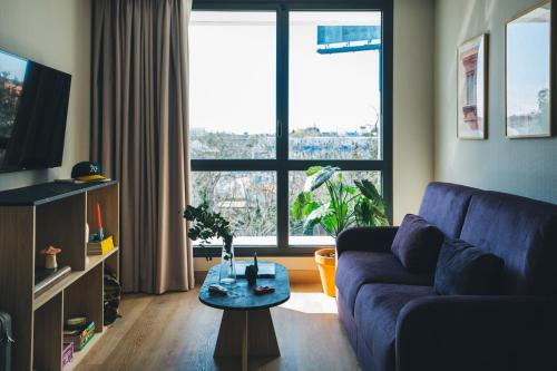 a living room with a blue couch and a large window at The Oliver Apartamentos Aravaca in Madrid