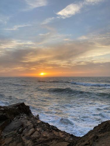 a sunset over the ocean with rocks in the foreground at Amaan ⴰⵎⴰⴰⵏ Cottage in Agadir