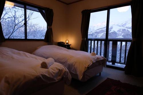 two beds in a room with two windows and a balcony at WAKURABA- Chalet with the best views in Hakuba! in Hakuba
