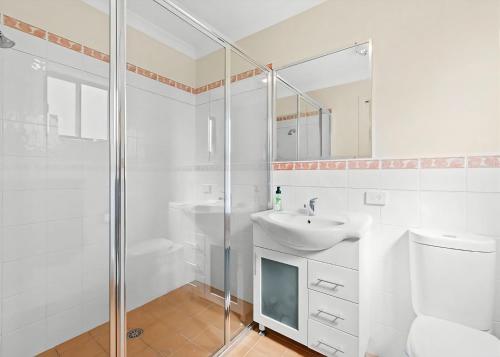 La salle de bains blanche est pourvue d'un lavabo et d'une douche. dans l'établissement Golfers Dream, à Batemans Bay
