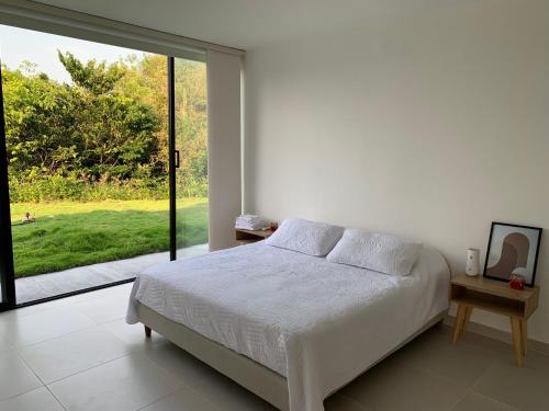 a white bedroom with a bed and a large window at Casa Sentido - Tu refugio campestre in Alvarado