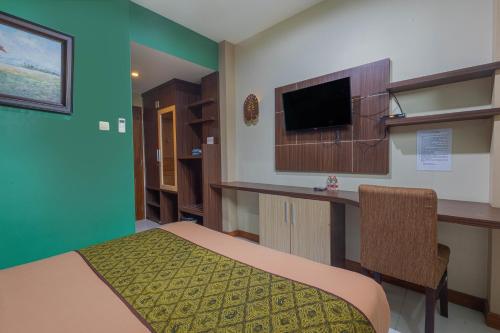 a room with a bed and a desk and a television at Hotel DMadinah inn Gentan in Solo