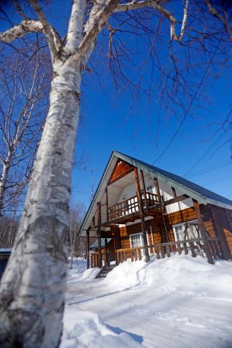 a log cabin in the snow next to a tree at The LODGE ABASHIRI in Abashiri