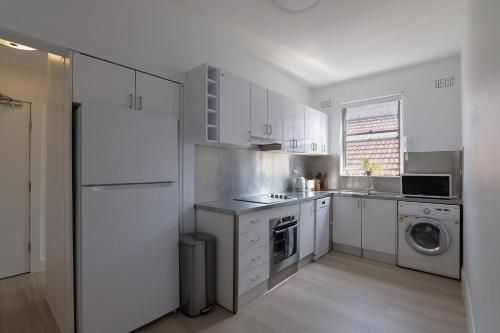 een keuken met witte kasten en een wasmachine en droger bij Bondi Beachfront Bliss in Sydney